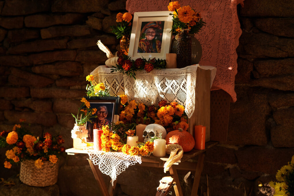 Traditional Janal Pixán altar with candles, marigolds, food, and framed photos of loved ones.
