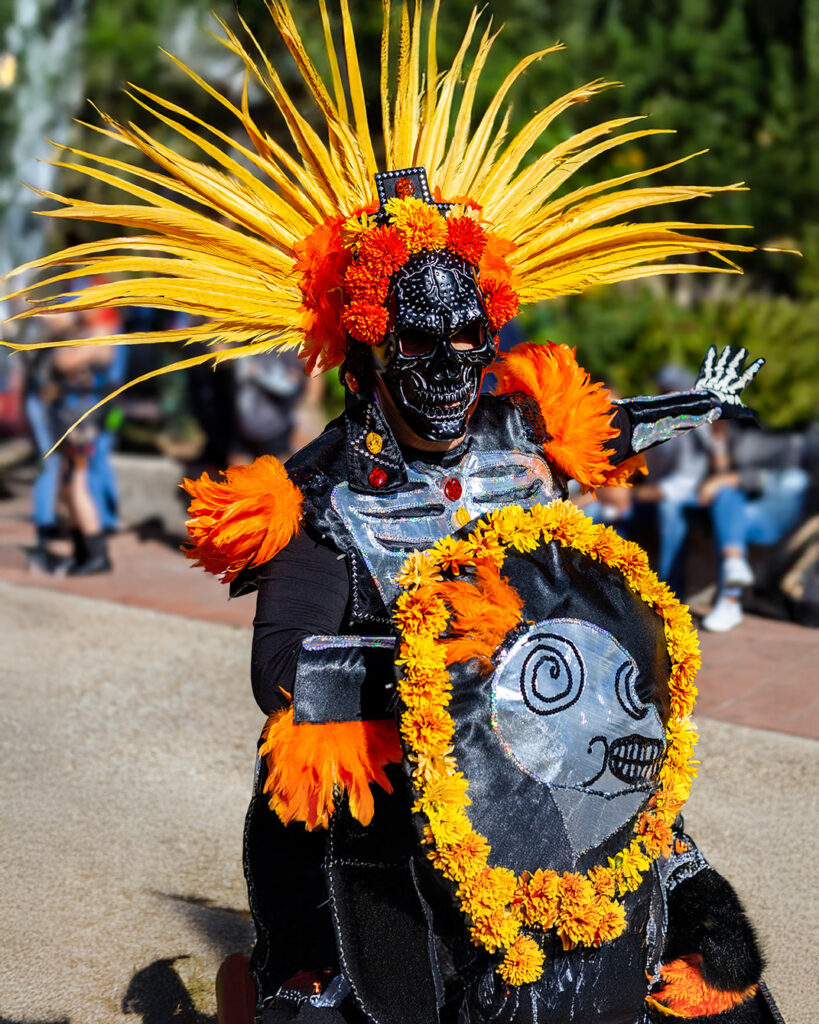 Person dressed in a vibrant Janal Pixán costume with yellow and orange feathers and marigold decorations.