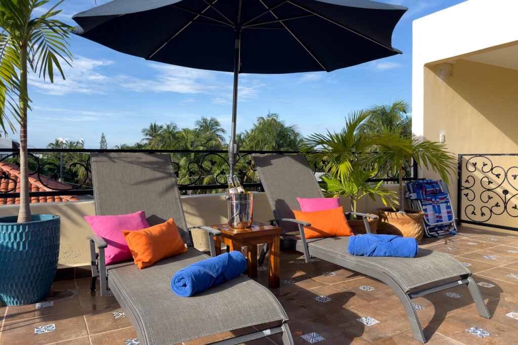 Private terrace with two lounge chairs, umbrella, and palm plants at Casa Catalina #3 in Puerto Morelos.
