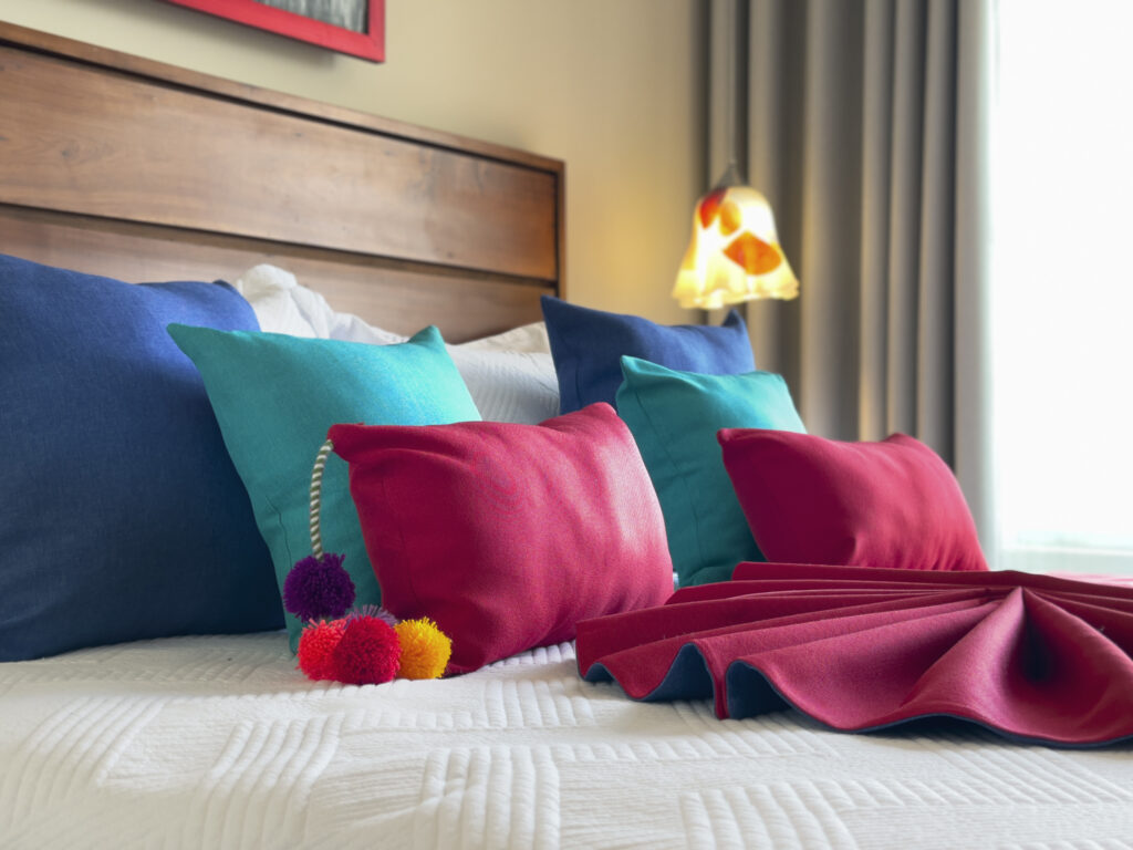Close-up of colorful pillows and folded linens on a king bed with soft lighting.