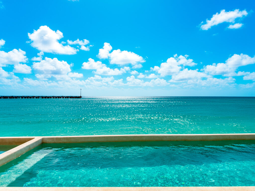 The building’s beachfront pool sits just steps from the sand, overlooking the calm turquoise water of Puerto Morelos. With lounge chairs, a tropical palm, and wide-open ocean views, it’s the perfect place to swim, relax, and soak in the beauty of the Caribbean coast.