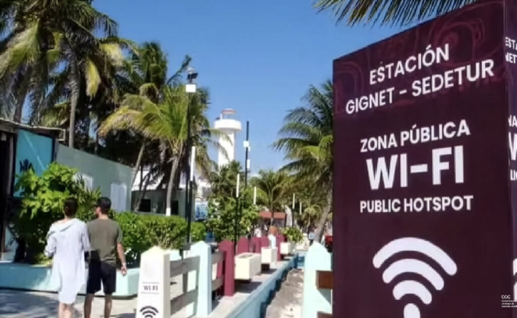 Public Wi-Fi hotspot sign on the Puerto Morelos waterfront walkway near palm trees and shops.