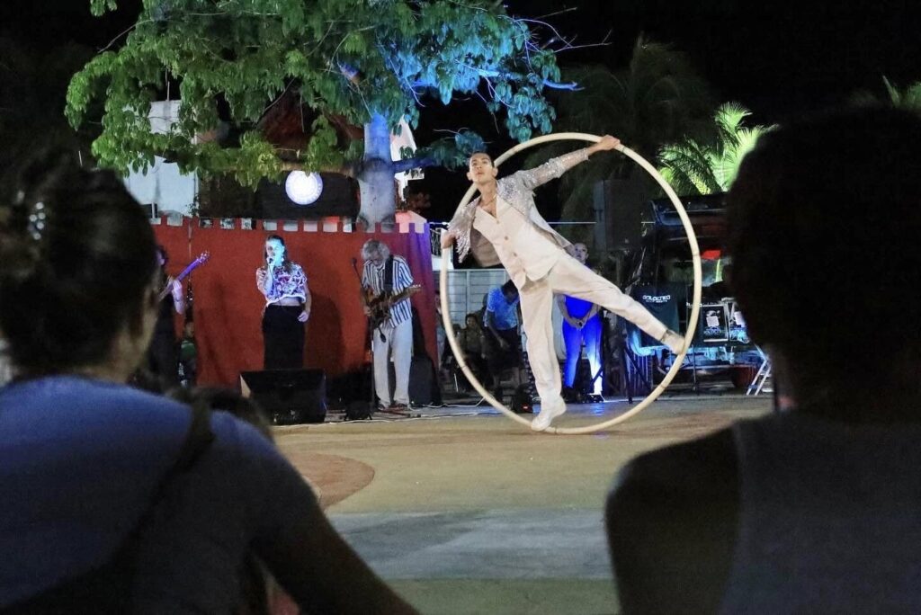 Performer balances inside a large Cyr wheel on an outdoor stage as spectators watch at night.