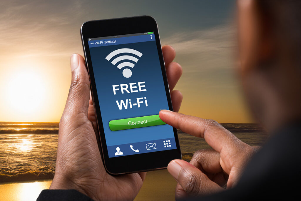 Hand holding a smartphone showing “FREE Wi-Fi” with a connect button, with the ocean in the background.
