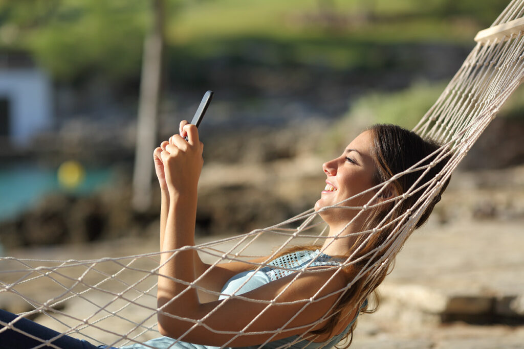Guest relaxing in a hammock outdoors while using a smartphone in the sunlight.