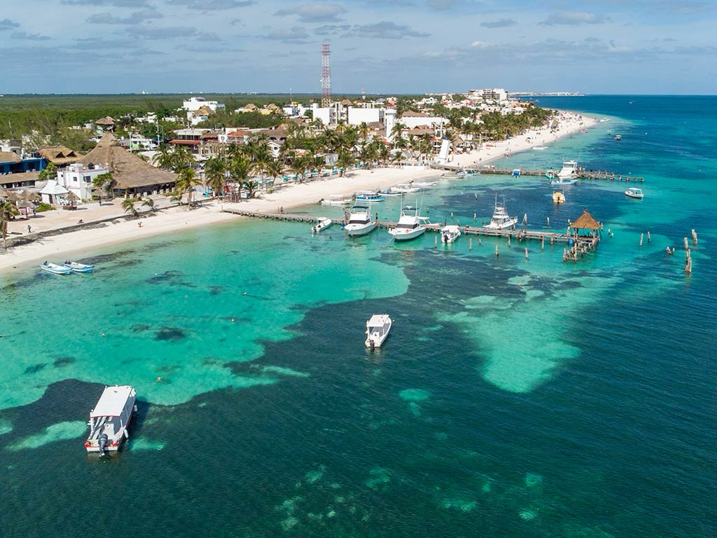 Aerial view of Puerto Morelos coastline, turquoise reef waters, and boats near the shore.