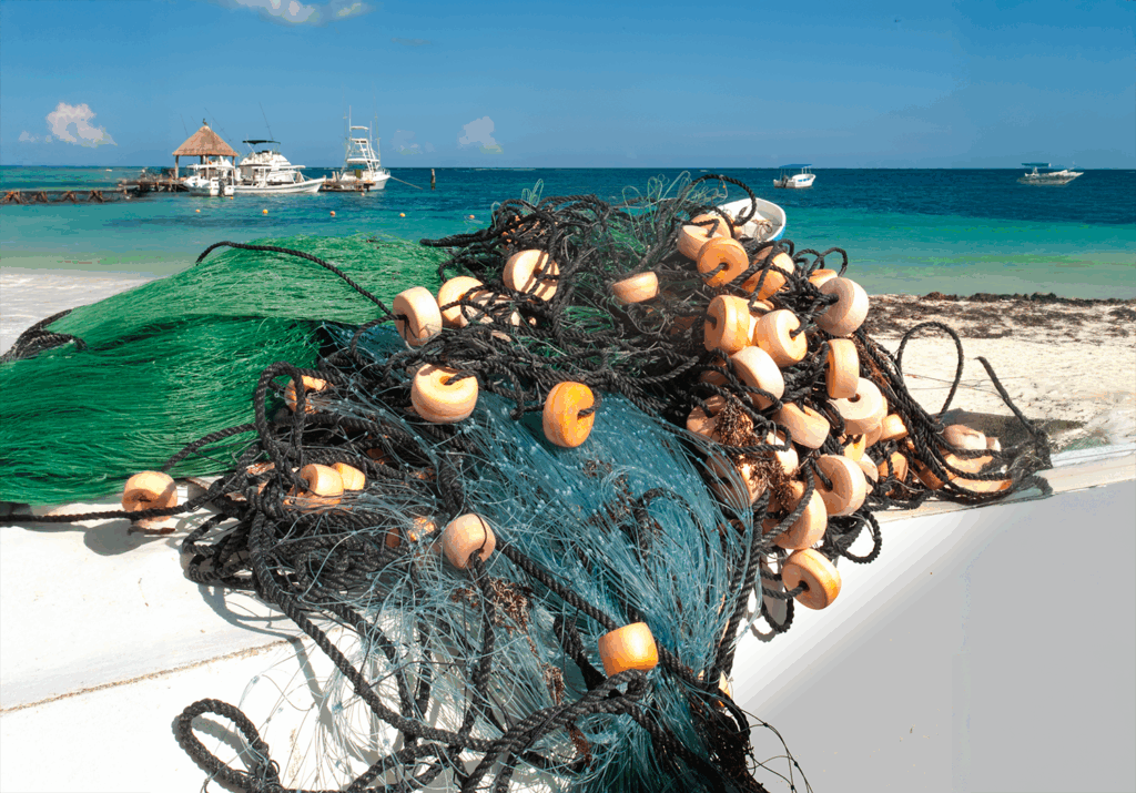 Fishing net with floats piled on a boat in Puerto Morelos, with turquoise sea and boats in the background.
