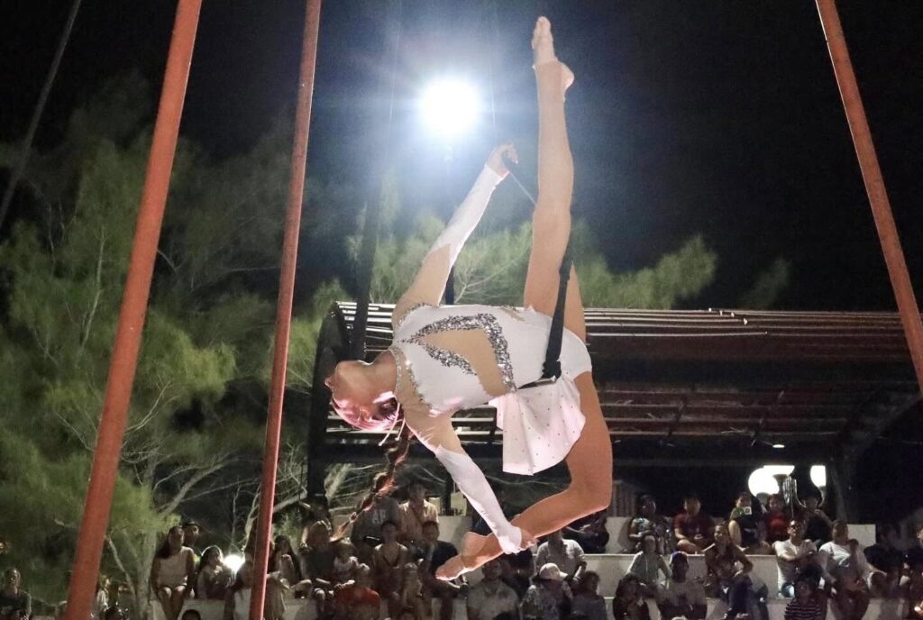 Aerial acrobat performs high above the crowd at night, lit by a bright spotlight.