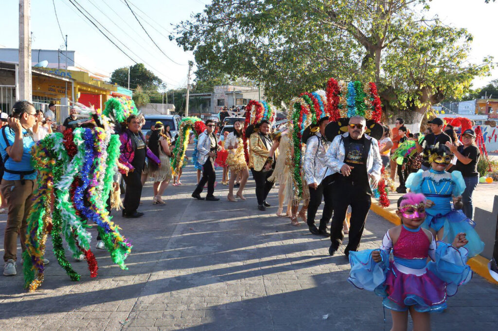 Dancers in bright tinsel costumes perform in the street as kids in blue and pink outfits watch during Carnival.