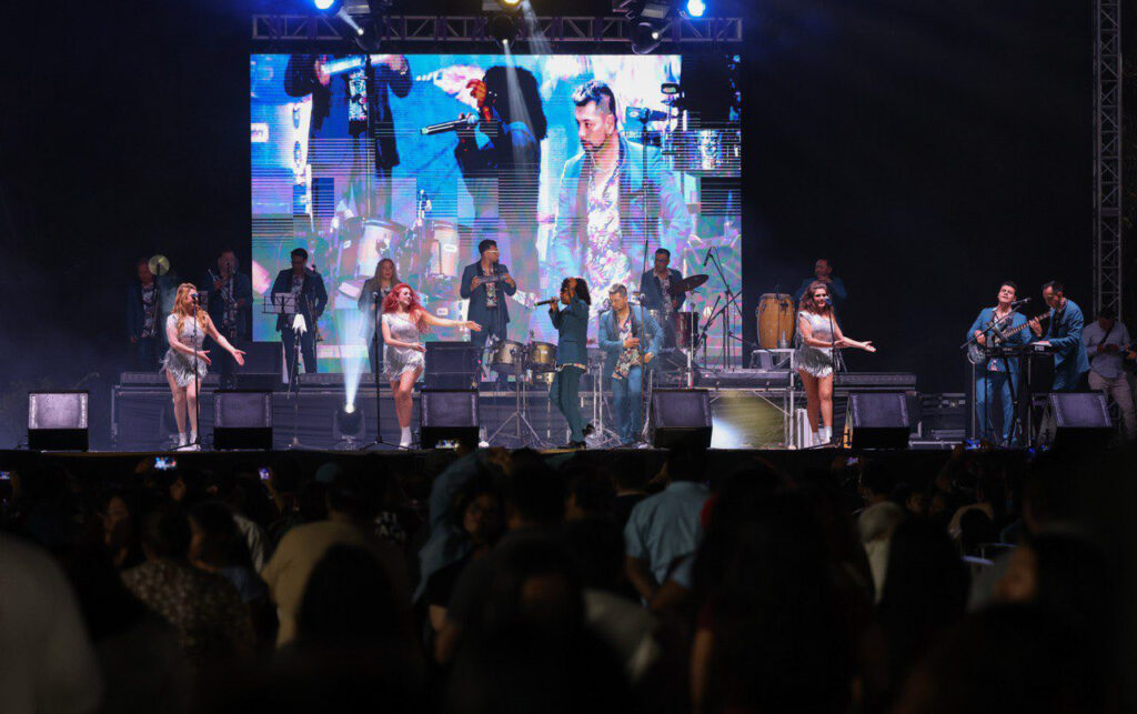 Live band performs on a brightly lit stage as a large crowd watches during Carnival week.