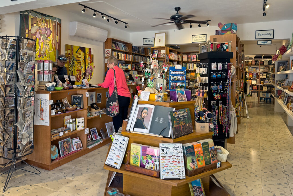 Inside Alma Libre Bookstore in downtown Puerto Morelos: a bright, welcoming space with a central display table, shelves of books stretching into the back, and local gifts and artisan items mixed throughout.