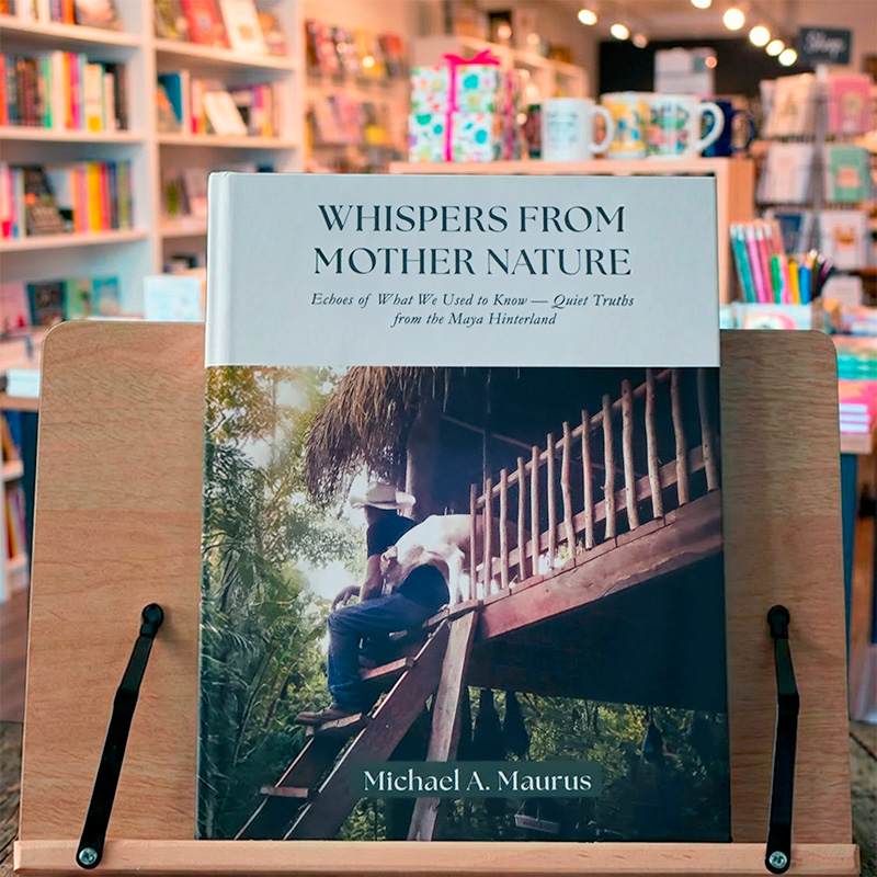 “Whispers from Mother Nature” displayed on a wooden stand inside a bookstore, with softly blurred shelves in the background.