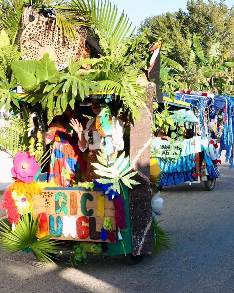A jungle-themed Carnival float with palm leaves and animal cutouts rolls down a road in Leona Vicario.
