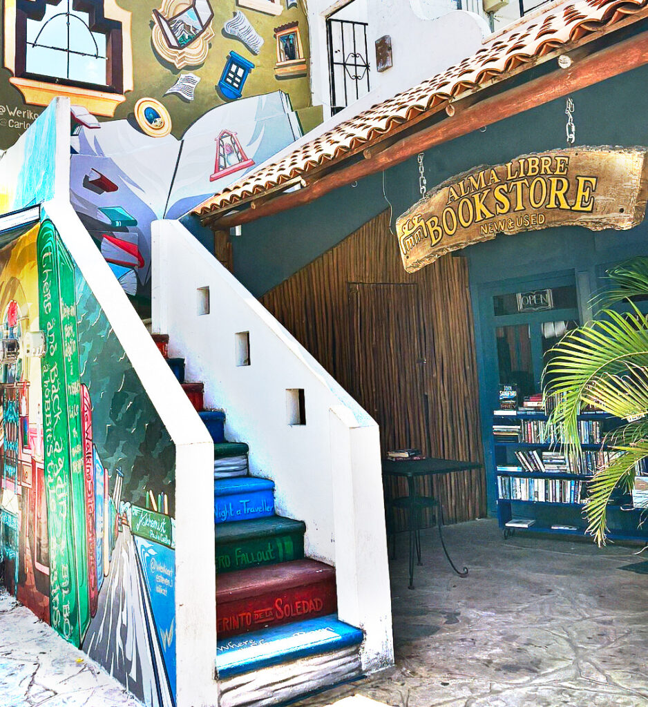 Colorful painted staircase beside a bright mural leading to the entrance of Alma Libre Bookstore in Puerto Morelos.