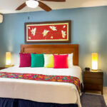 King bed with colorful pillows, bedside lamps, ceiling fan, and blue accent wall.