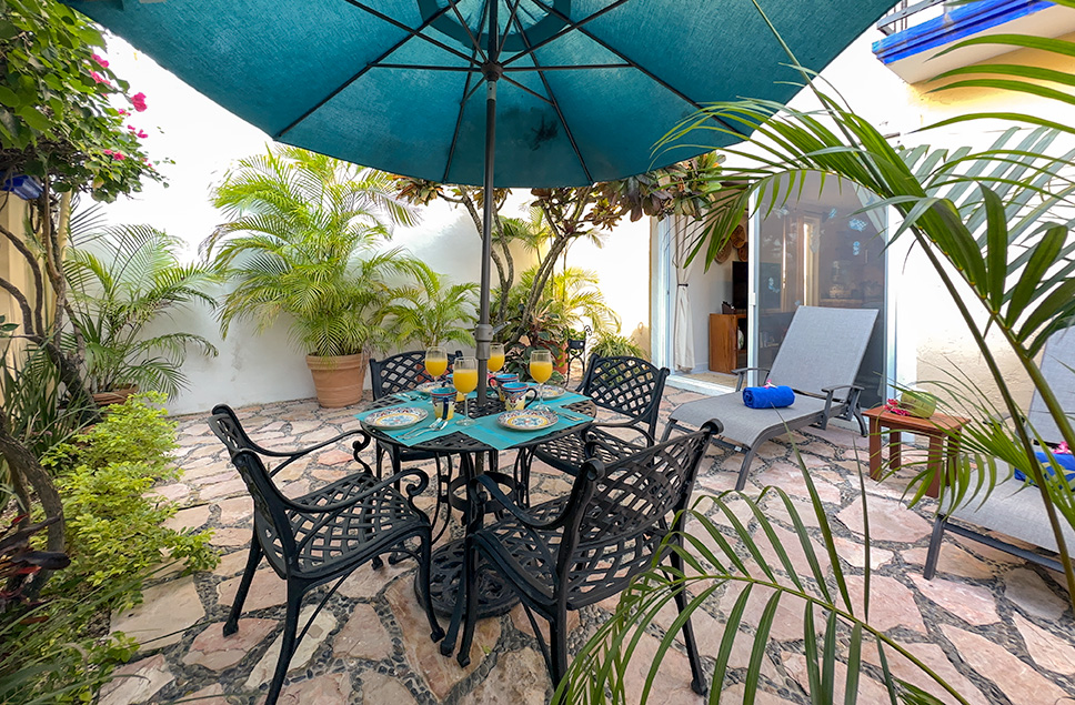 Private garden patio with umbrella dining table, chairs, and tropical plants at Abbey del Sol A2 – Apartment #9.