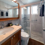 Bright bathroom with granite vanity, sink, toilet, and walk-in glass shower.