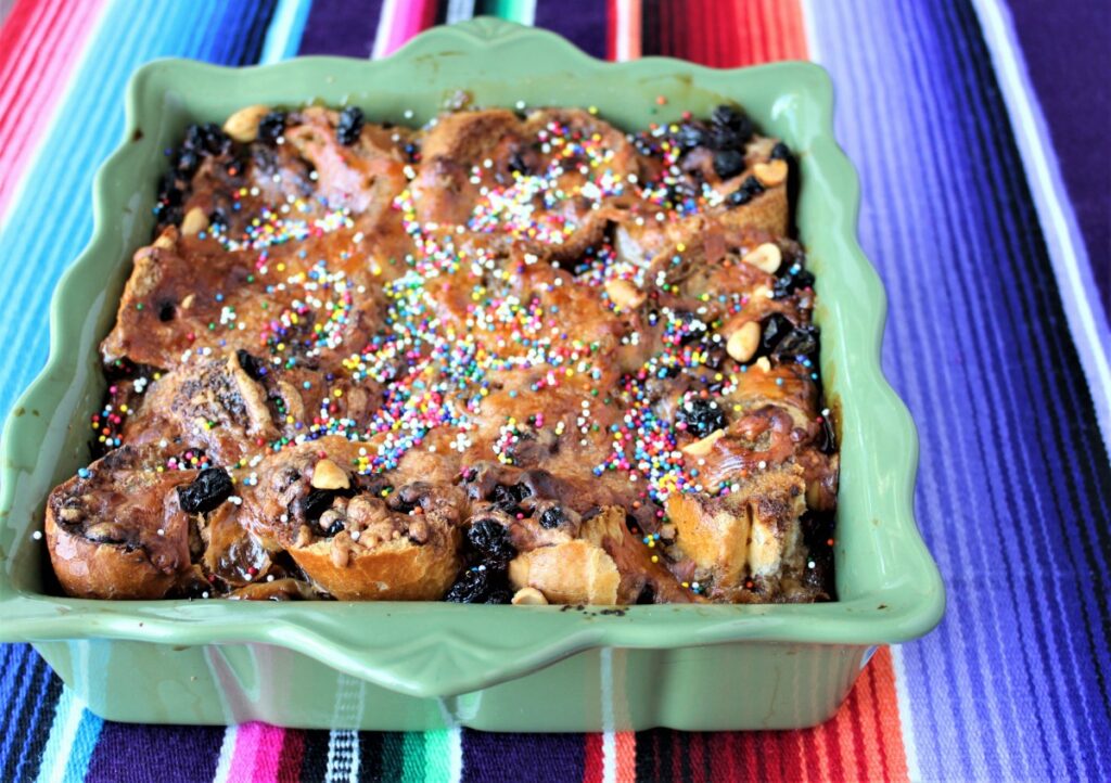 Traditional capirotada in a baking dish, topped with raisins, cheese, and colorful sprinkles.