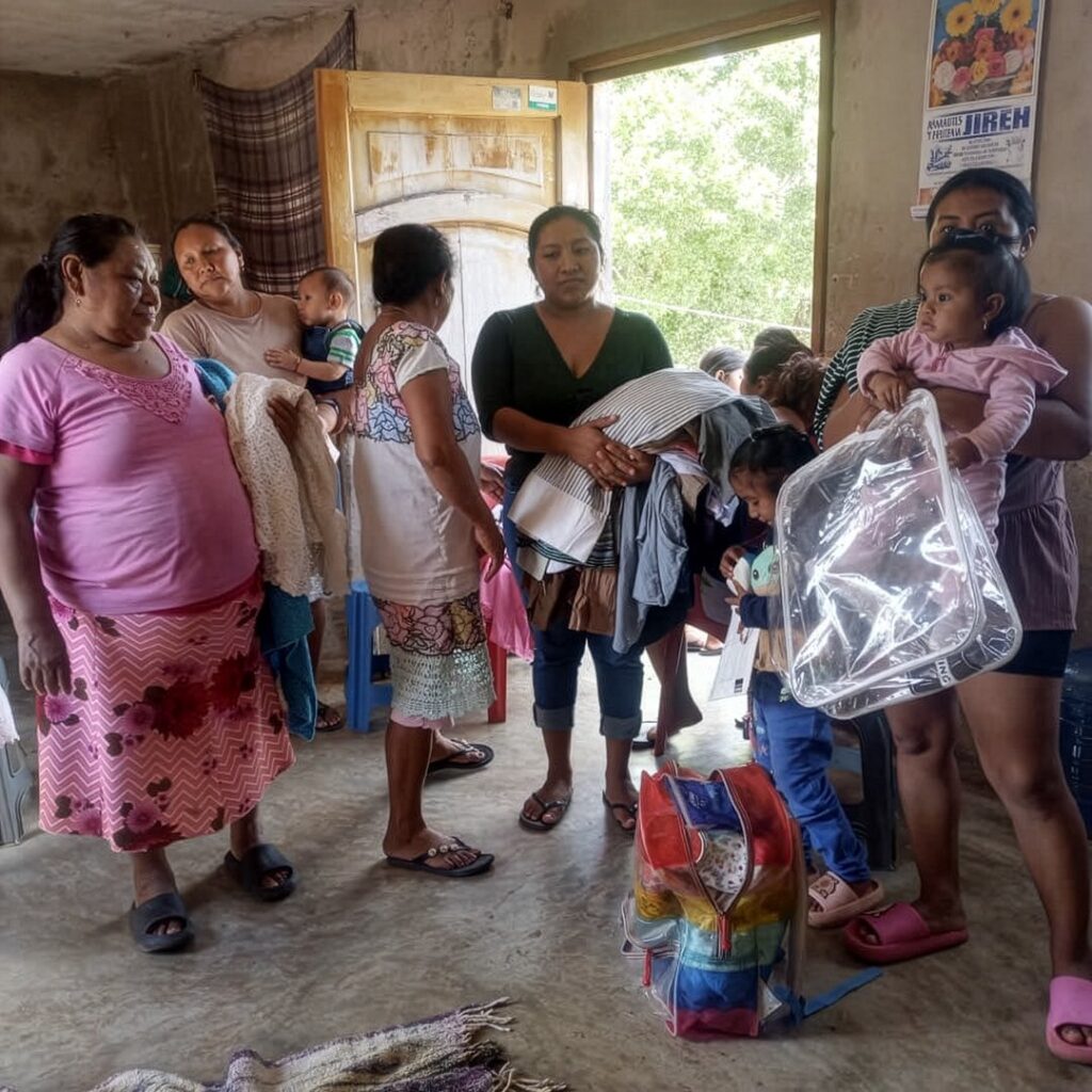 Women and children in a Maya village receive clothing and donated supplies during a community support visit.