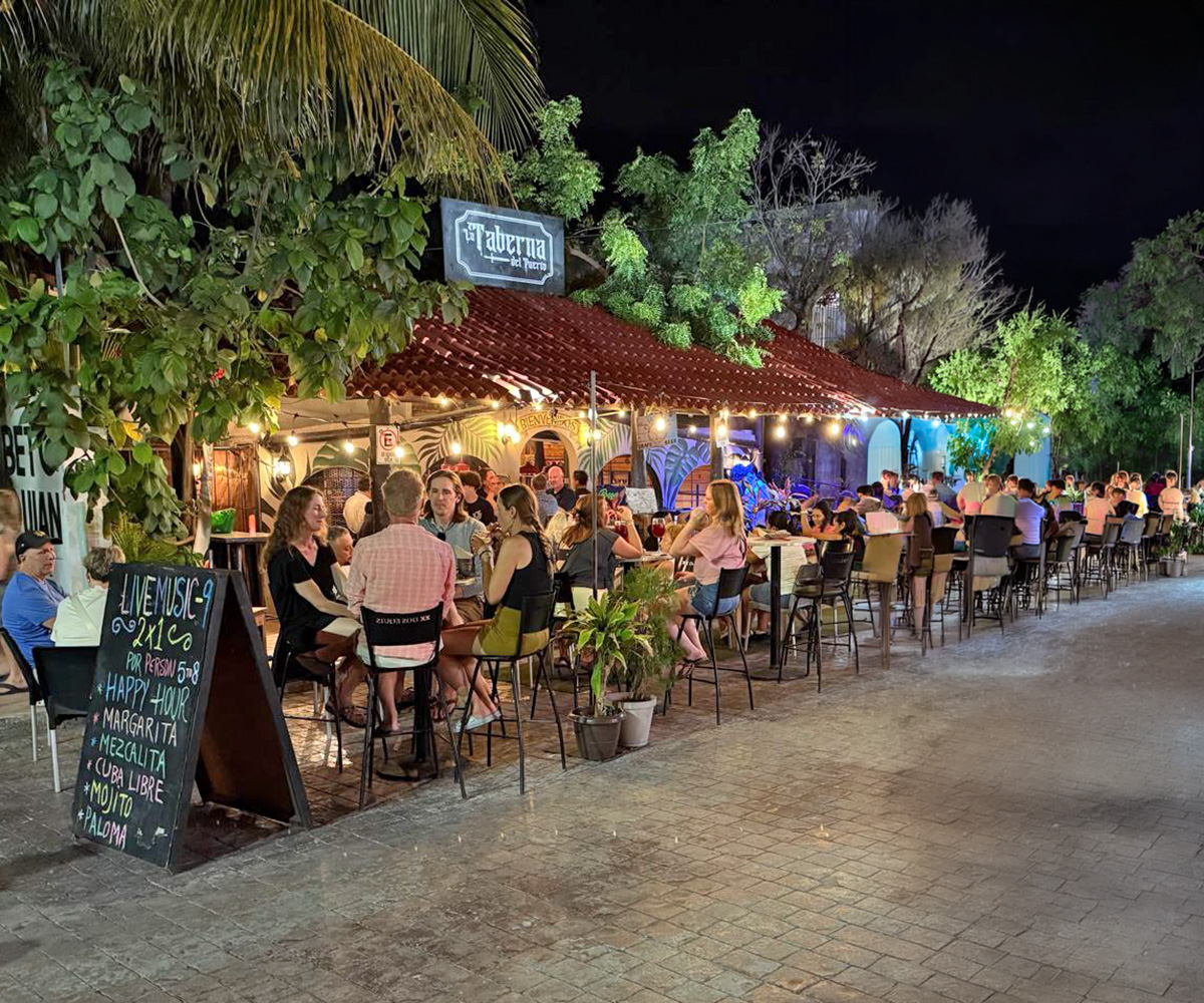 People dining outdoors beneath trees and lights in Puerto Morelos
