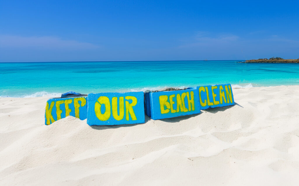 Keep Our Beach Clean message displayed in bright yellow and blue letters on white sand beside turquoise water