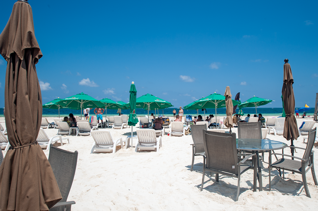 Beach chairs and tables set on white sand in Puerto Morelos under a bright blue sky