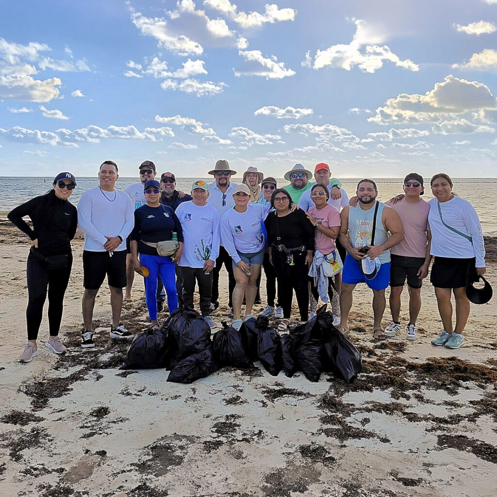 Community volunteers pose on the beach with bags of collected trash after a cleanup in Puerto Morelos