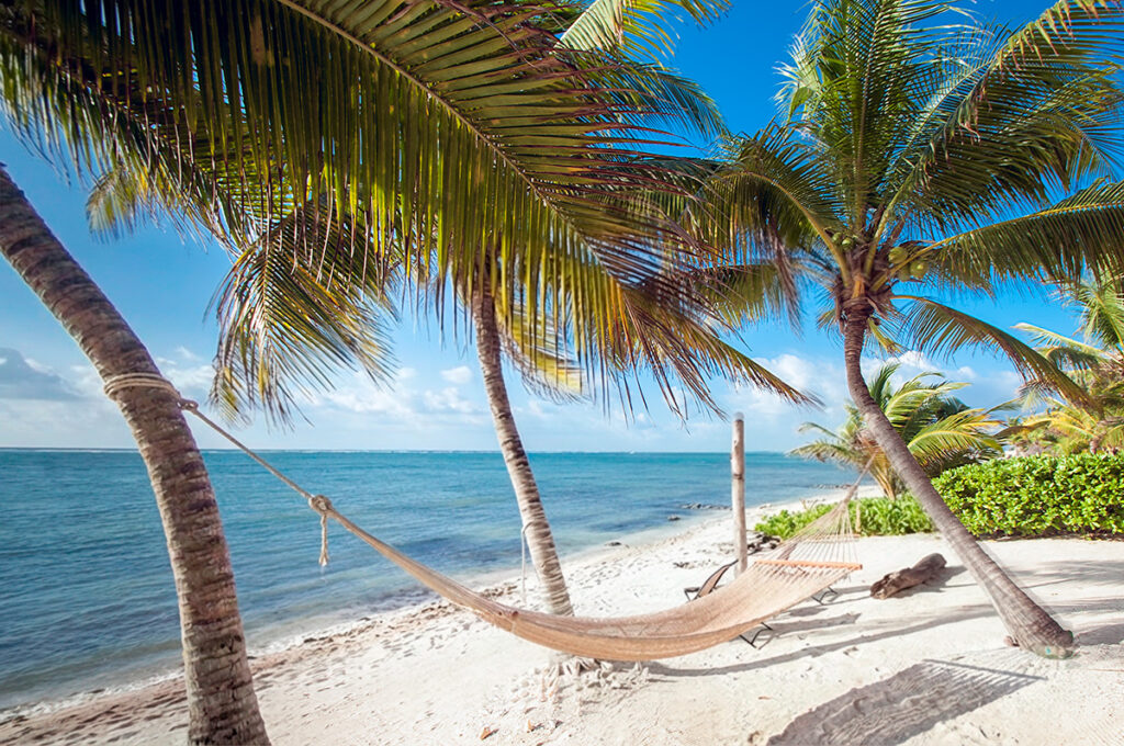 Hammock stretched between palm trees on a quiet sandy beach in Puerto Morelos