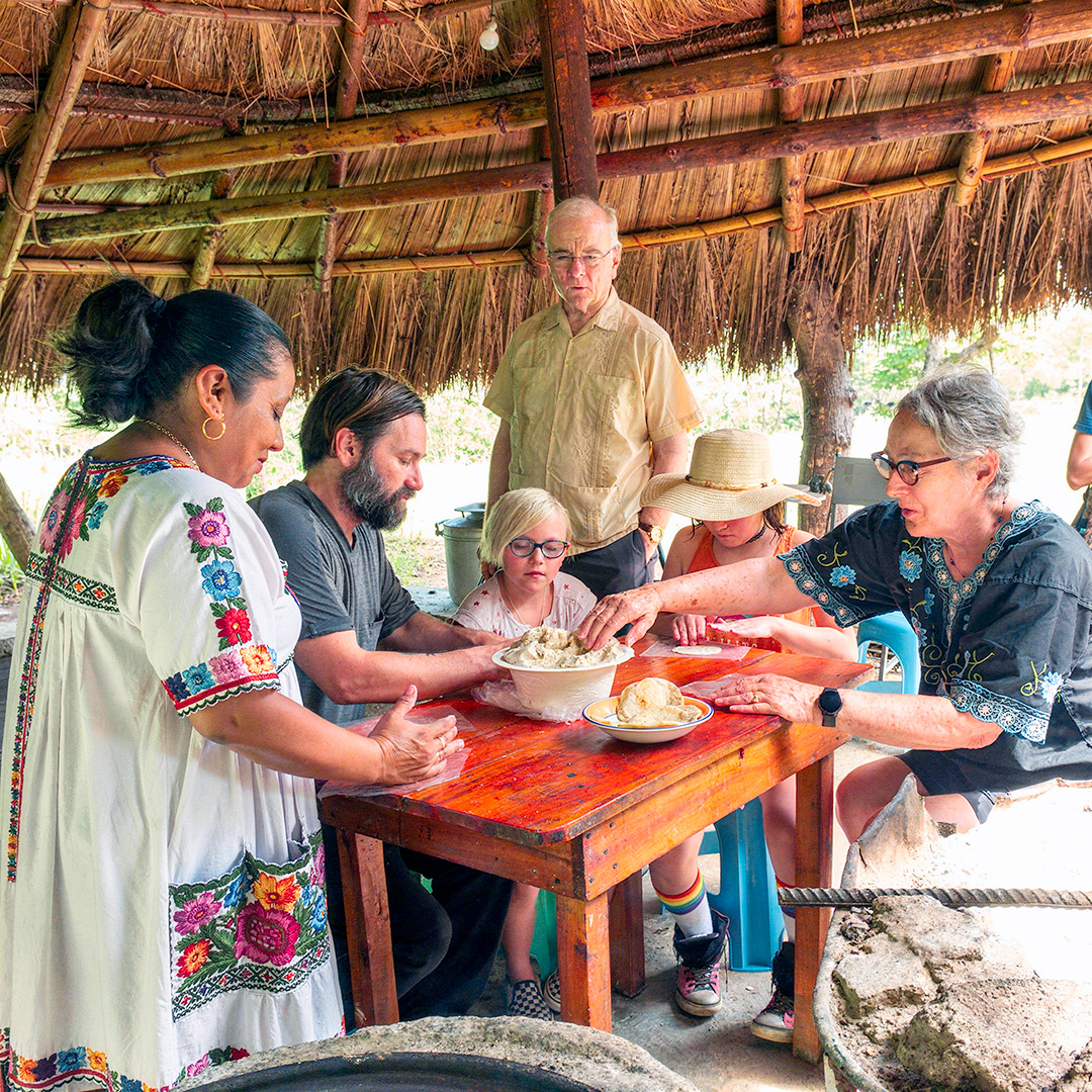 Visitors learning to make handmade tortillas with Maya hosts beneath a palapa