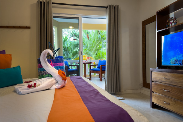 Bright king bedroom with TV, swan towels, and balcony doors opening to palm views.