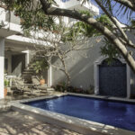 Exterior view of Casa Agua Azul, a Puerto Morelos vacation rental by Abbey del Sol, showing the gated entrance, balcony, palm tree, and bright Caribbean-style architecture.