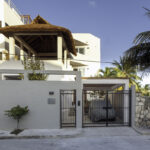 Exterior of Casa Agua Azul with balcony, palm tree, and gated entrance.