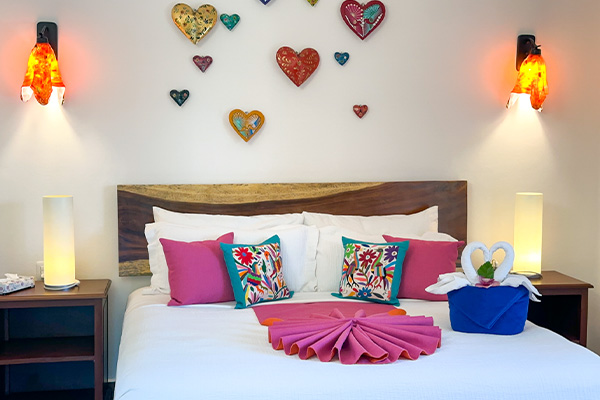 Catalina 2 bedroom with king bed, colorful pillows, heart wall decor, and warm lamps.
