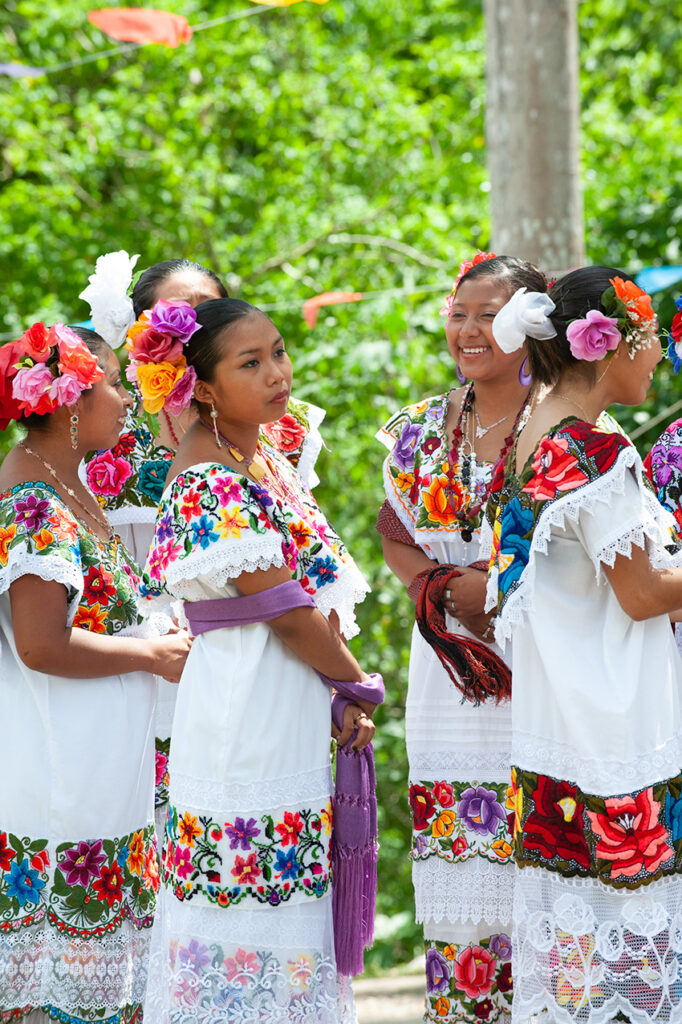 Young Maya women in embroidered dresses gather and smile during a community celebration near Puerto Morelos.