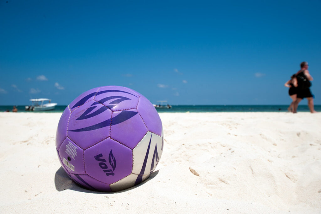 Purple volleyball resting on the white sand of Puerto Morelos beach.