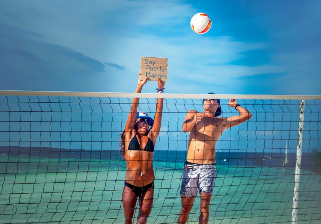 Alt text (≤100):
Beach volleyball players at the net on the shore of Puerto Morelos.