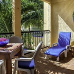 Private balcony at Apartment A#10 with table, chairs, lounge chair, and garden views.