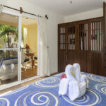 King bed in Apartment A#10 with towel art, wood wardrobe, and balcony doors.