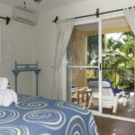 King bed in Apartment A#10 with balcony doors opening to tropical garden views.
