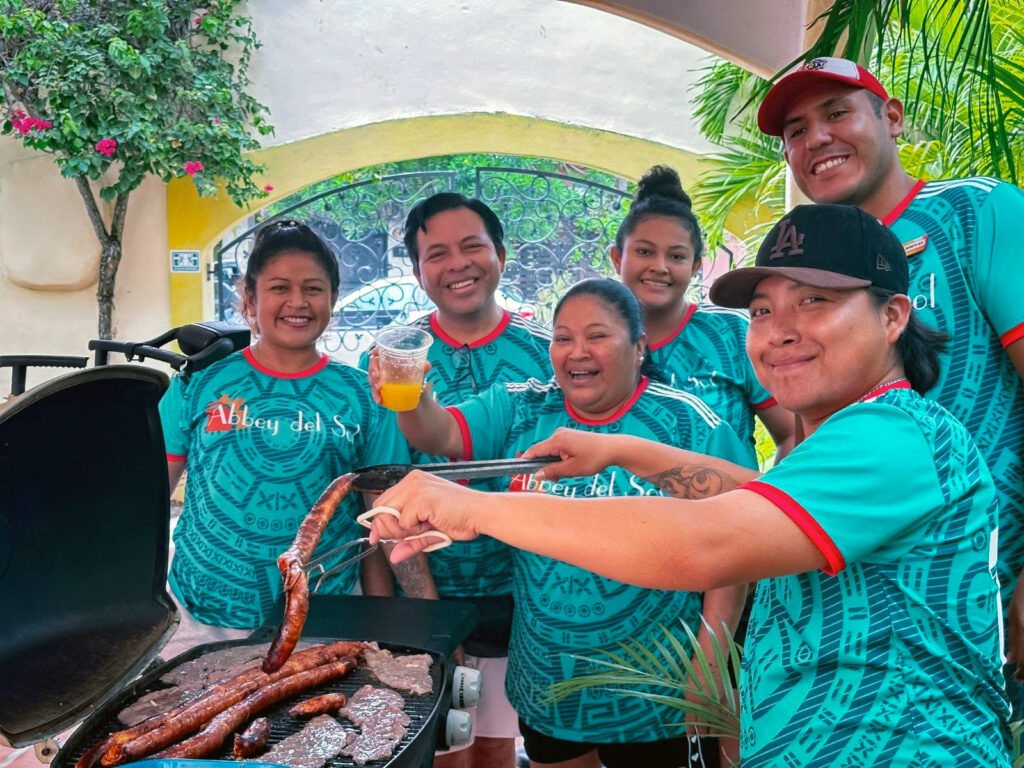 Abbey del Sol staff smiling together in green shirts while preparing food during World Cup celebrations.