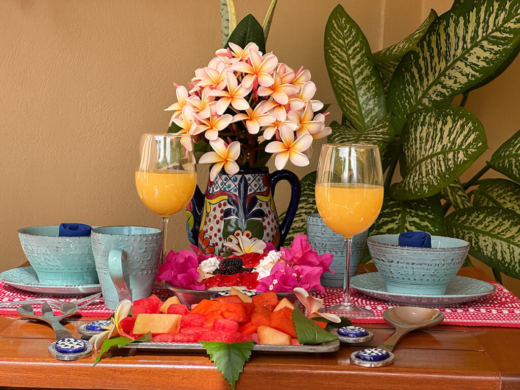 Colorful breakfast table with tropical flowers and fresh fruit on the balcony of Apartment #10 at Abbey del Sol 2.