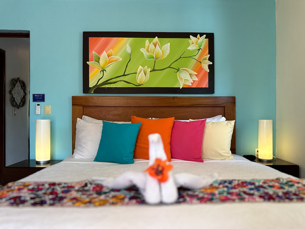 King bed with colorful cushions, tropical artwork, and towel decoration in Apartment #10 at Abbey del Sol 2.