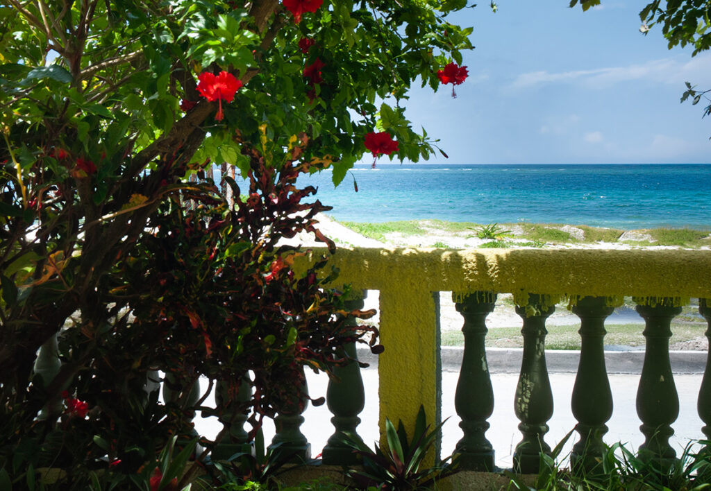 Beach view in Puerto Morelos framed by flowers, greenery, and a white balcony railing.