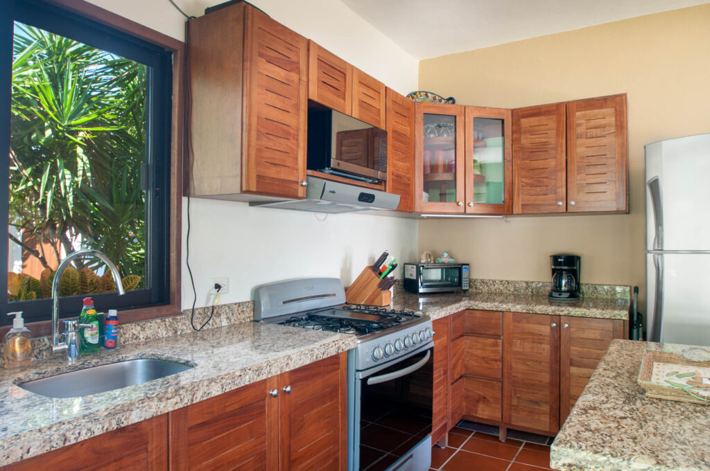 Kitchen sink beneath a garden window beside a stove, microwave, and wooden cabinets.