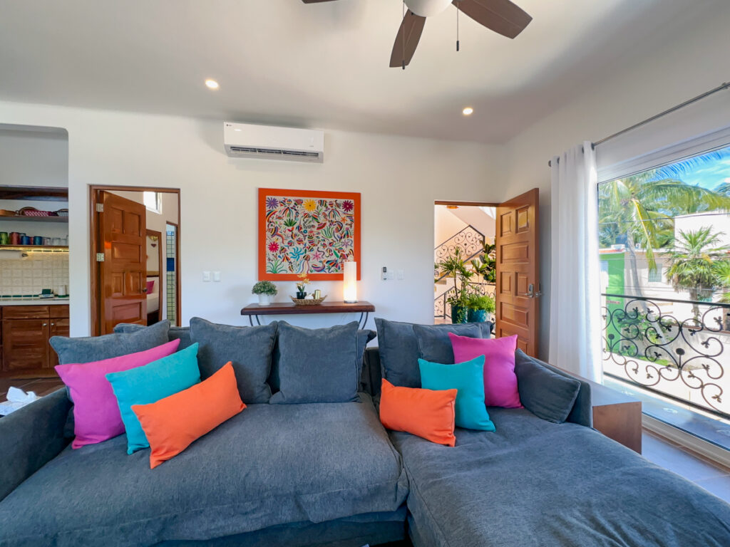 Large gray sectional beneath colorful artwork near an open wooden entrance door.