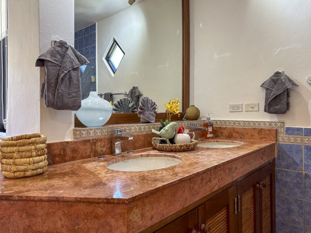 Long stone counter with two sinks above wooden cabinets beneath a wide mirror.