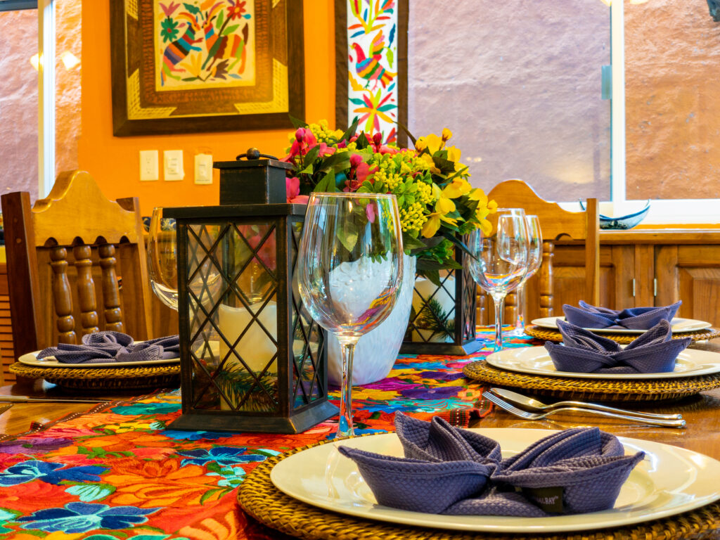 Plates, folded blue napkins, lanterns, and flowers arranged over a bright floral table runner.
