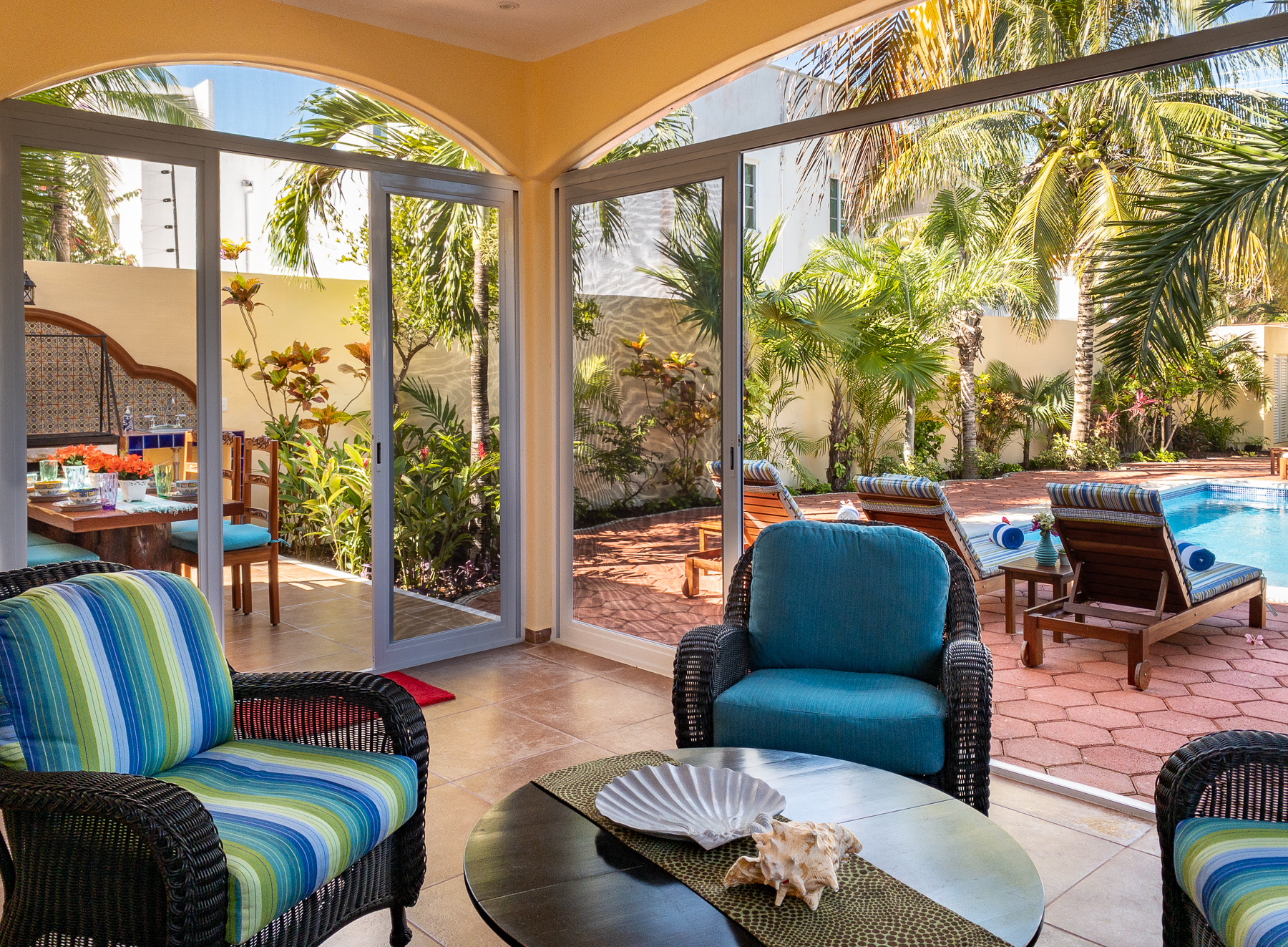 Wicker seating with blue and striped cushions around a round table in a screened patio beside the pool.