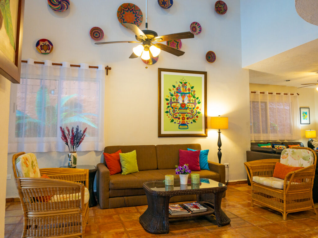 Sofa and wicker armchairs around a coffee table beneath colorful artwork and decorative plates.