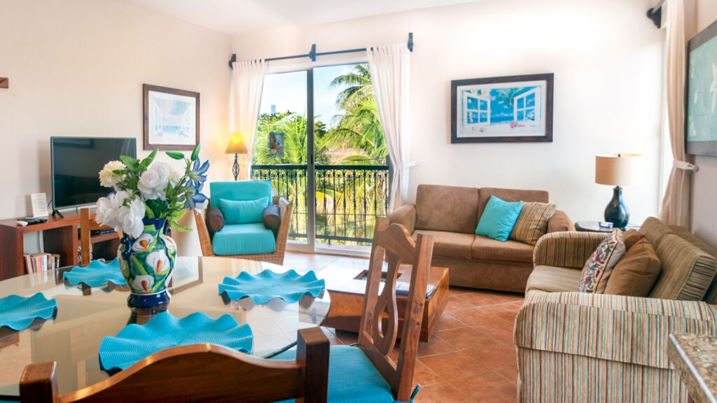 Dining table with blue napkins in front of a sofa, wicker chairs, and a balcony door.